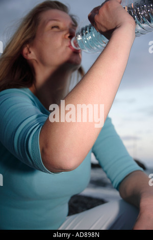 Giovane donna di bere acqua minerale da una bottiglia in spiaggia al tramonto Foto Stock