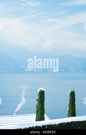 Cime di coperte di neve alberi e tetto, lakescape in background Foto Stock