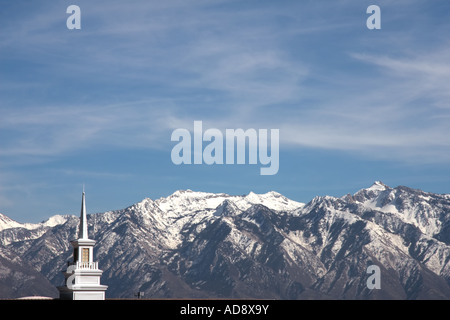 Una chiesa bianca steeple nella Salt Lake Valley, Utah, Stati Uniti d'America, con la coperta di neve montagne rocciose in background. Foto Stock