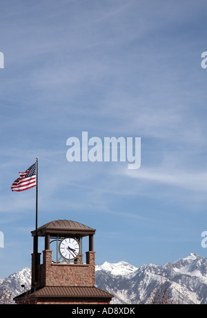 Un mattone di clock tower con una bandiera americana in SLC, Utah, Stati Uniti d'America, con la coperta di neve montagne rocciose in background. Foto Stock