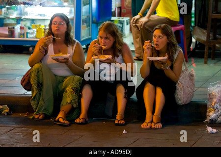 Tre viaggiatori femmina sedersi e mangiare cibo da asporto di notte, Khao San Road, Bangkok, Thailandia Foto Stock