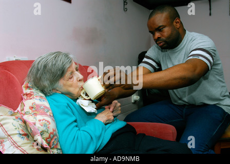 Membro del personale di cura assistere anziani residenti con acqua potabile presso la casa di cura per le persone con demenza, Londra, Regno Unito. Foto Stock