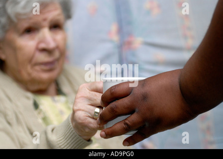 Membro del personale di assistenza che serve tè alla donna anziana in casa di cura per le persone affette da demenza, Londra, Regno Unito. Foto Stock
