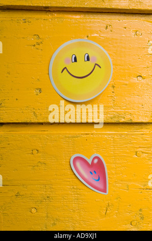 Due coloratissimi sorridenti faccia adesivi incollati a sfondo giallo Foto Stock