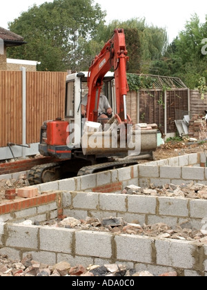 Nuova casa in costruzione mini escavatore immissione hardcore macerie sul sito di costruzione tra le pareti di casa nuova sottostruttura pronto per il pavimento di cemento REGNO UNITO Foto Stock