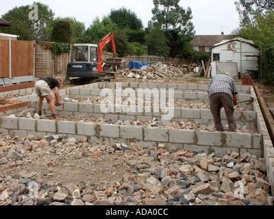 Operai a mano la rottura & hardcore di livellamento macerie intorno a muri di fondazione pronto per calcestruzzo soletta su nuova build casa unifamiliare Essex REGNO UNITO Foto Stock