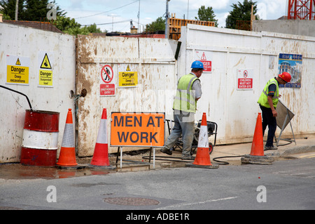 Due lavoratori in caschi di sicurezza e hi vis canottiere regolare la deviazione del traffico coni e segni al di fuori del sito di costruzione courtown Foto Stock