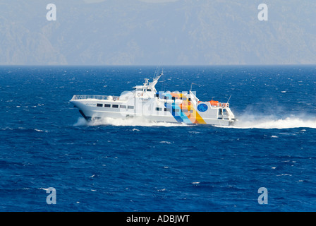 Vista orizzontale di un veloce catamarano per i passeggeri dei traghetti nel porto di scrematura attraverso la superficie del mare su una luminosa giornata di sole. Foto Stock