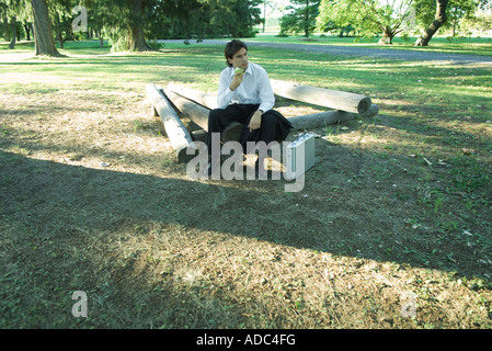 Imprenditore seduto su registri e una mela, guardando lontano Foto Stock