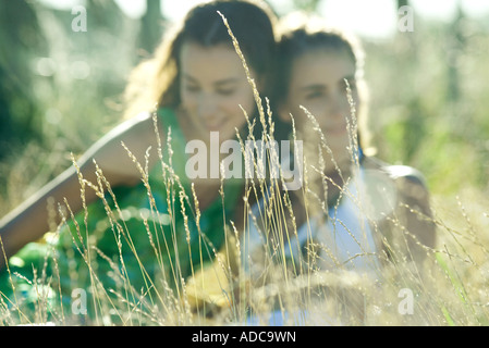Due giovani donne sedute in campo, concentrarsi sulle erbacce in primo piano Foto Stock