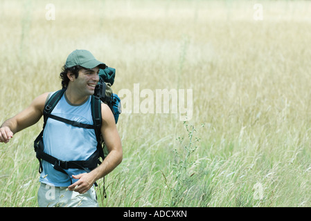 Giovane maschio escursionisti a piedi attraverso il campo, guardando lontano, sorridente Foto Stock