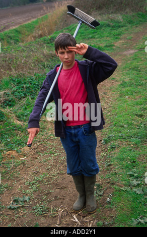 Ragazzo con una scopa e fingere di essere un soldato permanente per l'attenzione e salutando Foto Stock