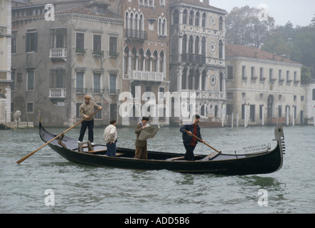 In una giornata grigia a Venezia un uomo il pendolarismo in gondola sul Canal si alza per leggere il suo giornale Foto Stock