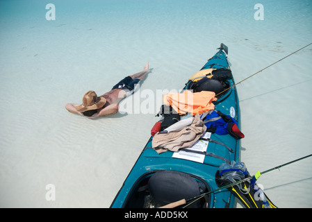 Un uomo si prende una pausa dal kayak e pesca a mosca per schiacciare un pisolino nel poco profonde acque tropicali delle isole Exuma Bahamas Foto Stock