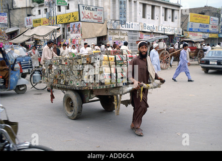 Uomo di Islamabad in Pakistan trascinando il rimorchio caricato con vuoto lattine di olio attraverso la strada affollata Foto Stock