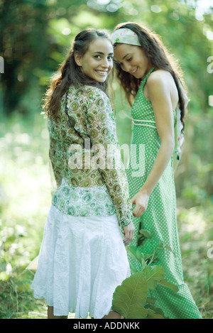 Due giovani donne in piedi nei boschi, uno guardando sopra la spalla in telecamera Foto Stock