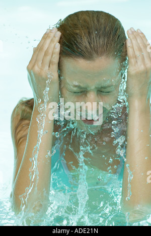 Giovane donna in piscina, schizzi viso con acqua Foto Stock