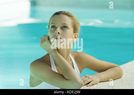 Donna che indossa halter costume da bagno, testa e spalle, appoggiata sul bordo della piscina Foto Stock