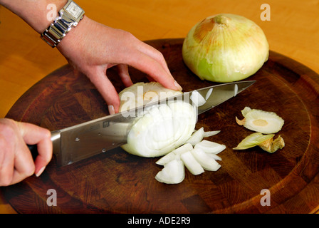 Donna di mano azienda coltello da cucina e tritare una cipolla gialla su un tagliere. Foto Stock