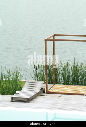 Sedia a sdraio sul ponte tra la piscina e il corpo di acqua Foto Stock