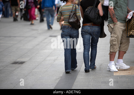 Due giovani donne in jeans che trasportano le borsette a piedi passato uomo in pantaloncini corti e formatori sul marciapiede in oconnell street Foto Stock