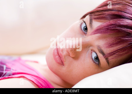 Bella donna caucasica giacente su una crema di divano in pelle e occhi blu corto capelli rossi Foto Stock