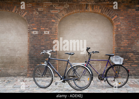 Due biciclette stette in piedi contro un muro di mattoni di Copenhagen, Danimarca. Foto Stock