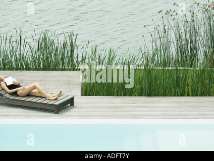 Donna sdraiata su poltrona accanto al lago, dormendo con libro sul petto Foto Stock