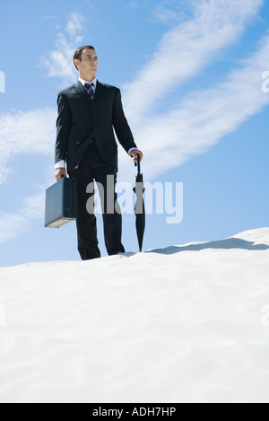 Imprenditore permanente sulla duna, valigetta di contenimento e ombrello a basso angolo di visione Foto Stock