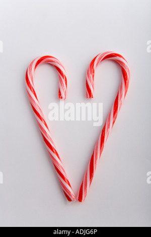 Primo piano di due Natale candy canne in forma di cuore sfocato in alto su sfondo bianco ritratto in studio Foto Stock