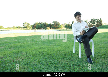 Imprenditore seduto in poltrona, sul prato, leggendo il giornale e azienda mug Foto Stock