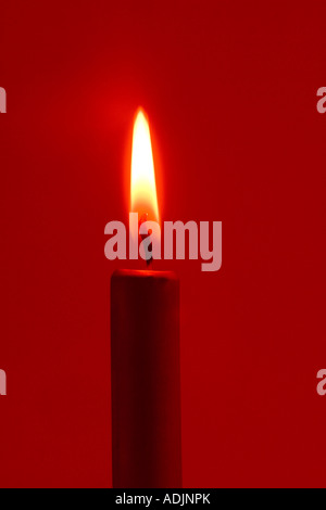 Primo piano della golden accesa christmas candle on dark sfondo rosso ritratto in studio Foto Stock