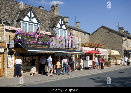 I turisti in visita nei piccoli negozi di Main Street Bourton sull'acqua Costwolds REGNO UNITO Foto Stock