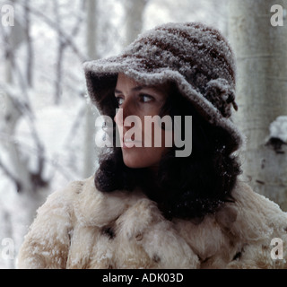 Attraente giovane donna in tempesta di neve vestito calorosamente nel coniglio pelliccia e cappello di lana nuova neve si aggrappa al suo cappello e il cappotto Foto Stock