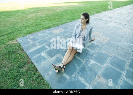 Imprenditrice seduta a terra sul patio, tenendo i documenti Foto Stock
