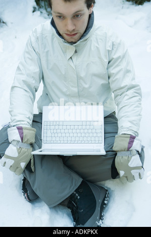 Giovane uomo seduto nella neve, laptop in giro Foto Stock