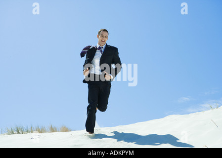 L uomo a indossare giacca e cravatta in esecuzione attraverso dune, ridendo Foto Stock