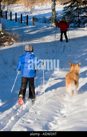 Due giovani ragazze sci di fondo come il golden retriever corre lungo con loro Ely Minnesota inverno Foto Stock