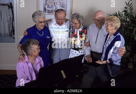 Gruppo di anziani amici amicizie in piedi riuniti intorno ad un pianoforte e canto noi usa stati uniti america pov Foto Stock