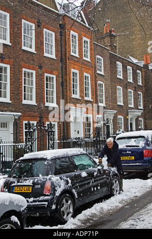 L'uomo raschia neve off Mini Cooper auto parcheggiate in London street Chiesa fila Hampstead Inghilterra REGNO UNITO Foto Stock