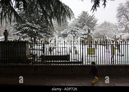 Ragazzo giovane passeggiate passato coperta di neve cimitero London Regno Unito Foto Stock