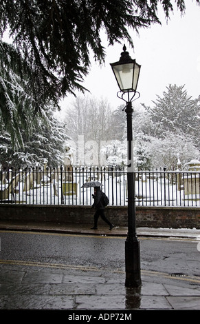Donna con ombrello passeggiate passato coperta di neve cimitero Hampstead North London Regno Unito Foto Stock