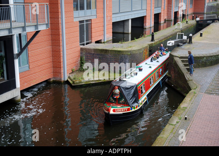 Canal lunga barca passando attraverso blocchi nel centro di Birmingham con appartamenti moderni in background Foto Stock