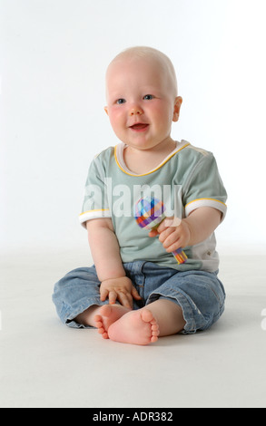 Felice bambino seduto sul pavimento con un sonaglio Foto Stock