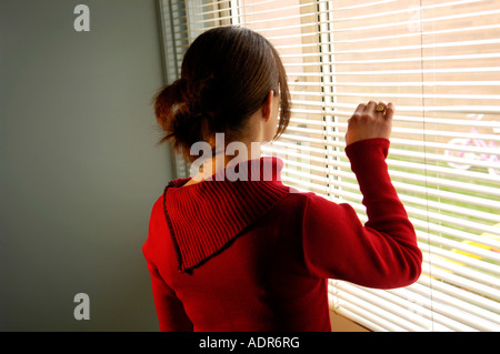 Silhouette di donna giovane di guardare attraverso una finestra con persiane Foto Stock