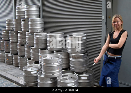 Cameriera avente pausa sigaretta davanti di serrande e barili di birra. Southwark, Londra, Inghilterra Foto Stock