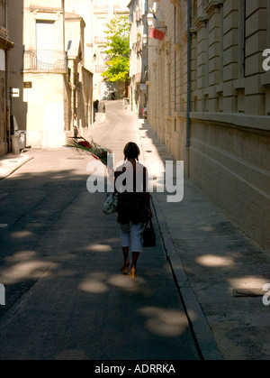 Una donna sola si allontana giù per una strada tenendo un mazzo di fiori Foto Stock