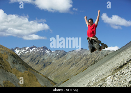 L'uomo saltare giù pendio roccioso con le braccia sollevate Foto Stock