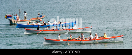 Fuori Charlestown Shoreline equipaggio misti vogatori in tre squadre lungo pilota gig row barche sotto gli ordini di partenza gara fuori mare e ritorno Cornovaglia Inghilterra UK Foto Stock