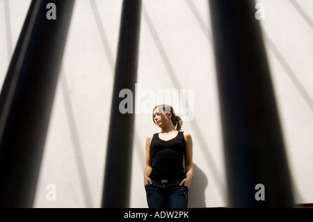 Giovane donna in interni con le ombre di colata di windows forme grafiche sulla parete dietro il suo aspetto di una prigione o gabbia Foto Stock